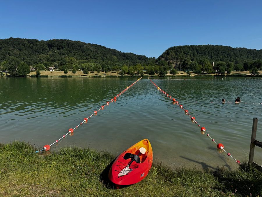 Un kayak rouge sur la berge du lac de Champos, lignes de bouées et collines boisées