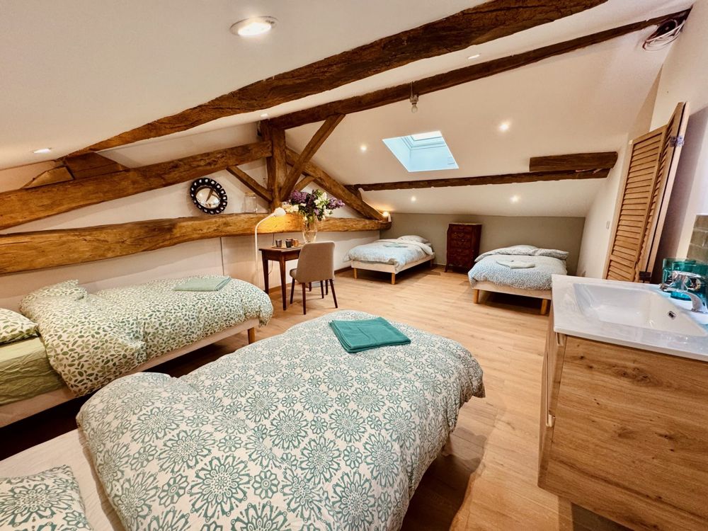 Grande chambre aux poutres apparentes, avec quatre lits simples, velux, bureau et lavabo