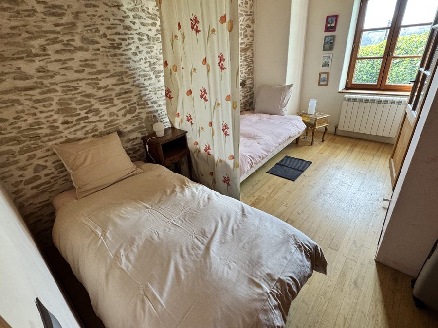 Chambre de deux lits séparés par un rideau fleuri, mur de pierre