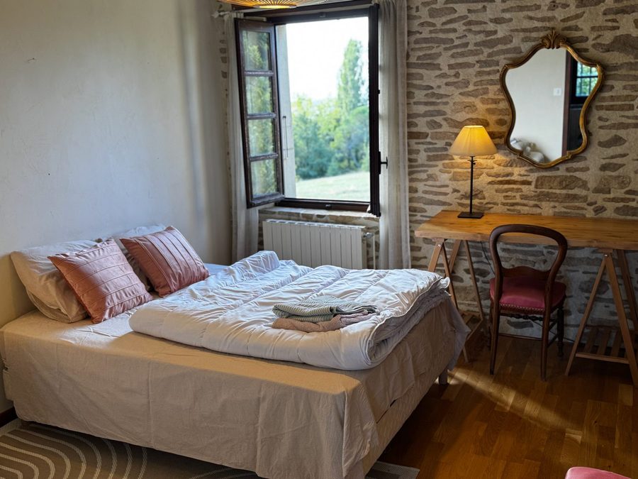 Chambre au lit double avec coussins roses et fenêtre ouverte sur le parc