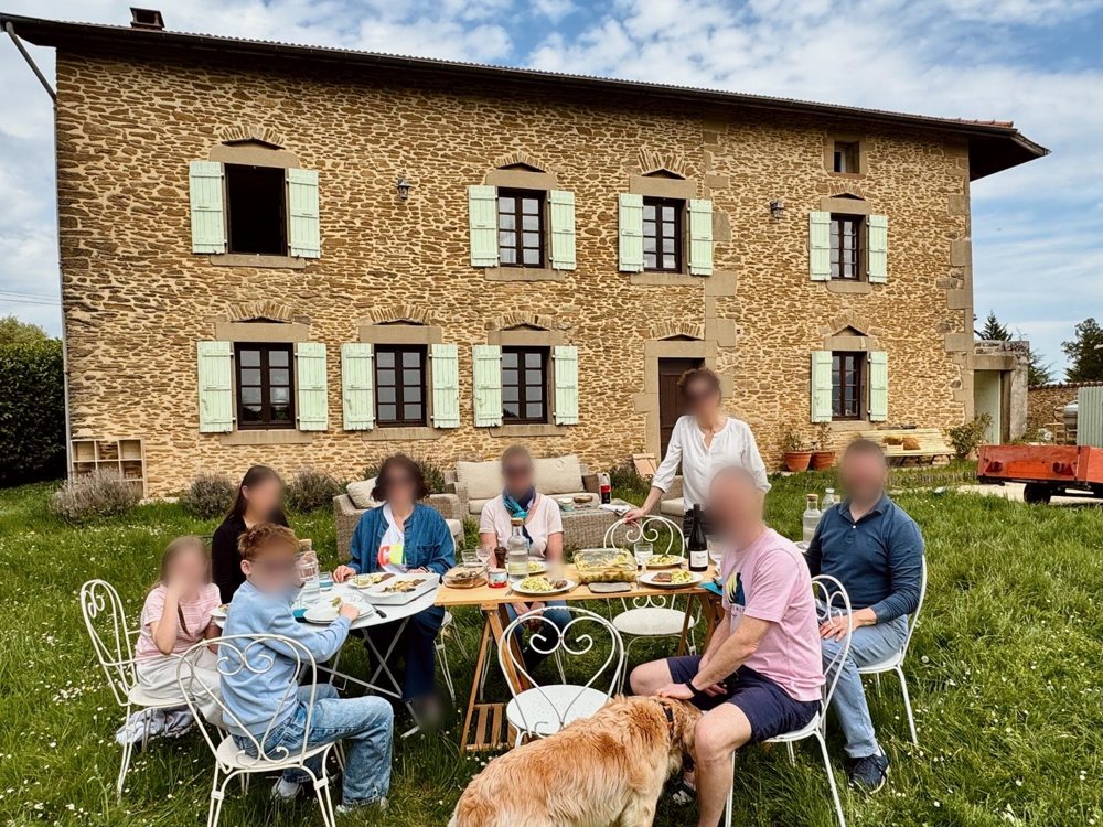 Une famille déjeune sur l'herbe devant la maison, le chien au premier plan