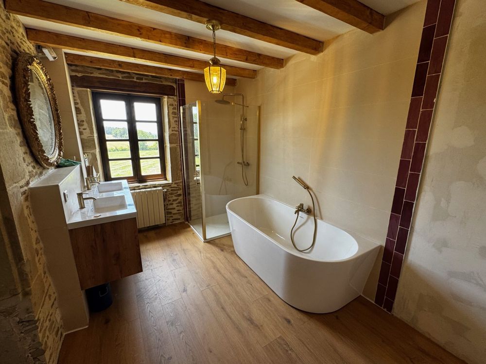 Salle de bain rénovée de la suite parentale, baignoire îlot, poutres et fenêtre sur la campagne