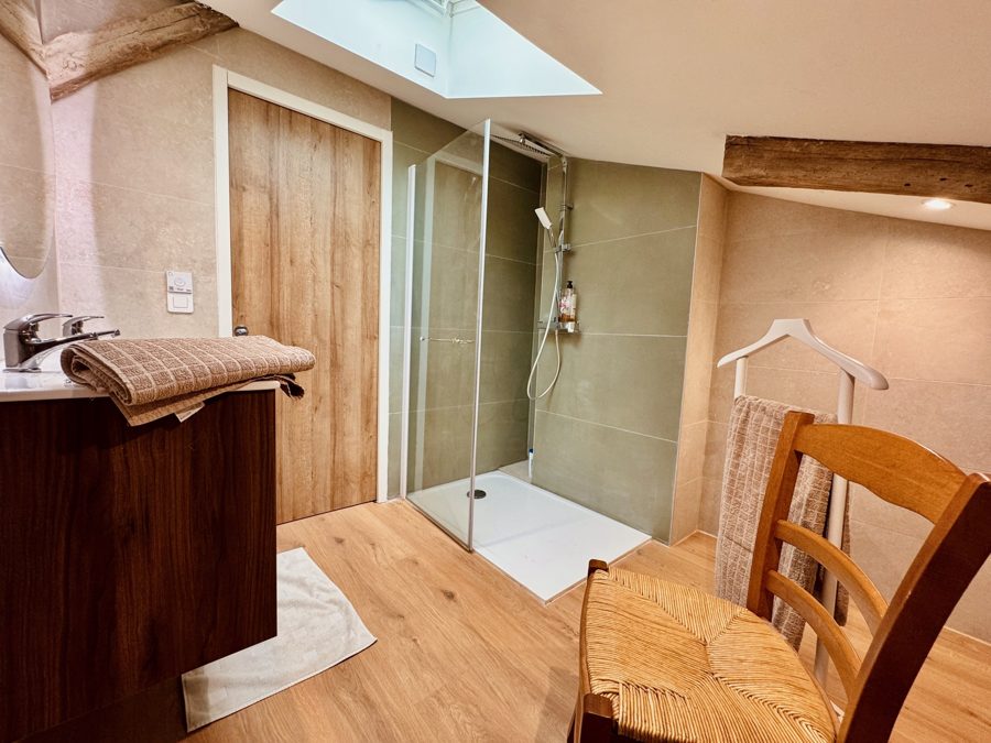 Salle d'eau avec douche vitrée, porte en bois et chaise paillée