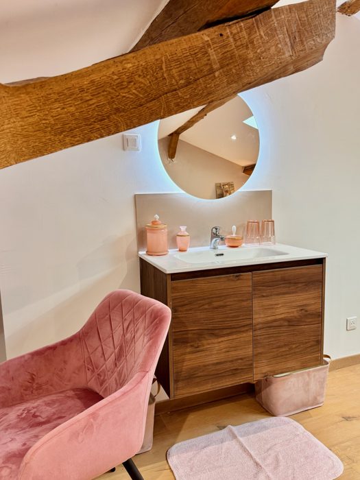 Vasque sur meuble en bois, miroir rond et fauteuil rose