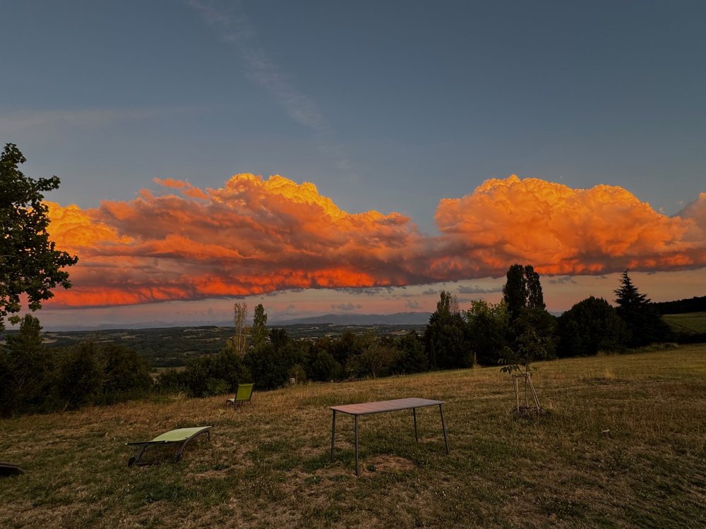 Bande de nuages orange au couchant au-dessus de la prairie et d'une table de jardin
