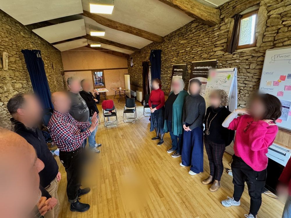 Une vingtaine de participants debout en cercle dans la grande salle aux murs de pierre